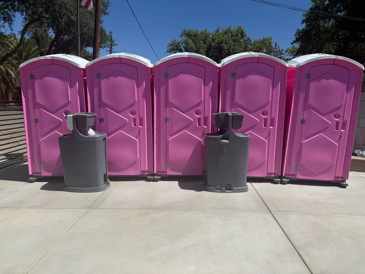 Pink porta potties lined up beside portable hand-washing stations
