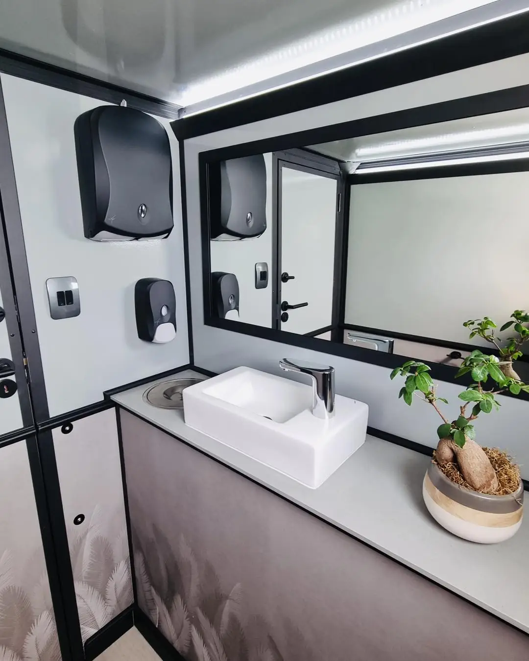 Restroom trailer interior with a vanity sink, faucet and mirror