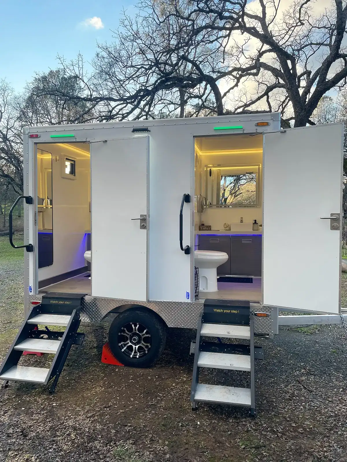 Restroom trailer at dusk with doors open and lights glowing inside