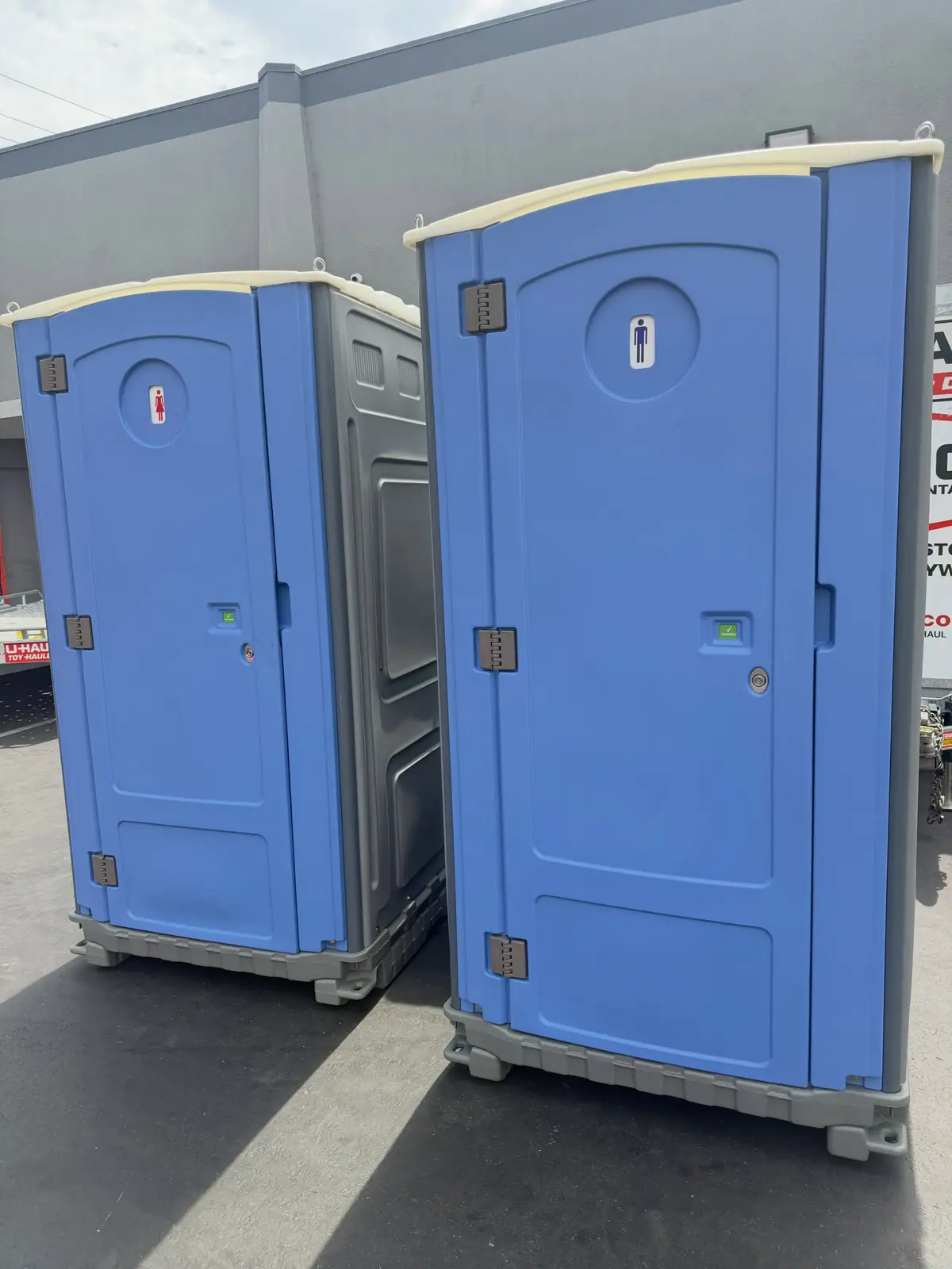 Two blue standard porta potties side by side on a parking lot