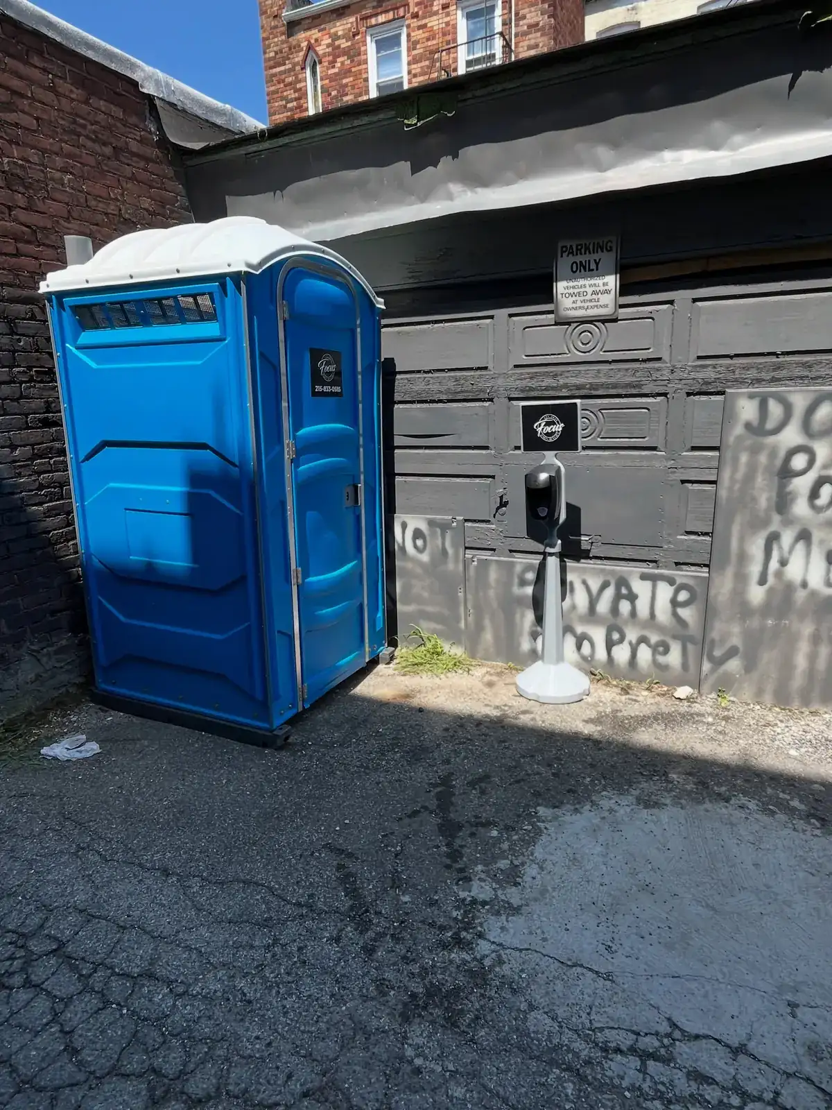 Blue portable toilet placed on pavement in a narrow side alley