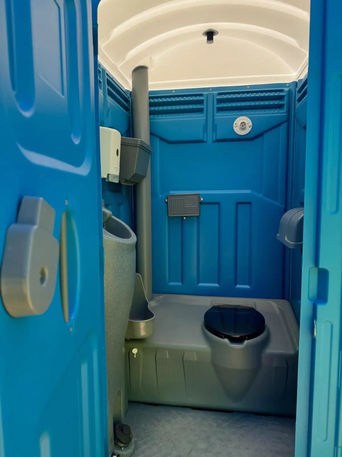 Inside a standard porta potty showing the urinal and vent pipe