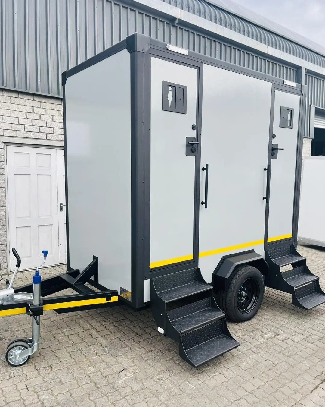 White two-stall restroom trailer parked on a level lot with steps at the doors